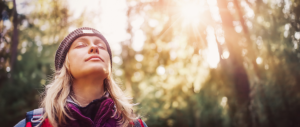 A spiritual woman in a beanie, mesmerized by the sun's rays, peacefully standing amidst the woods.