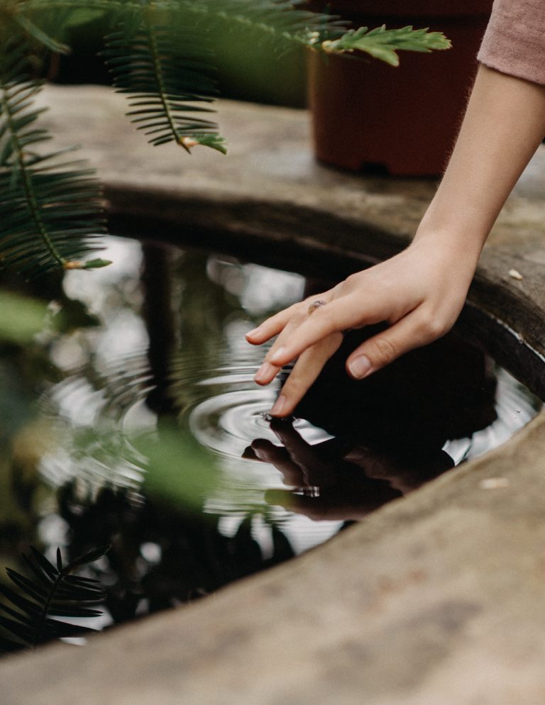 A woman's spiritual hand reaching into a pond.
