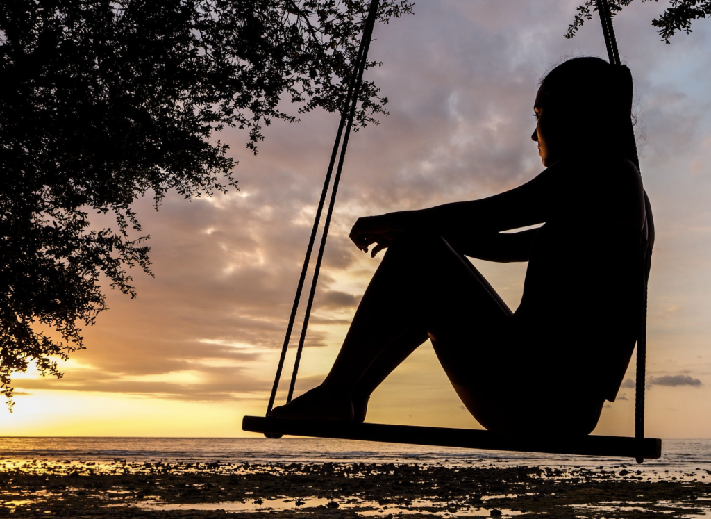A silhouette of a woman sitting on a swing at sunset, surrounded by a hypnotic and spiritual atmosphere.